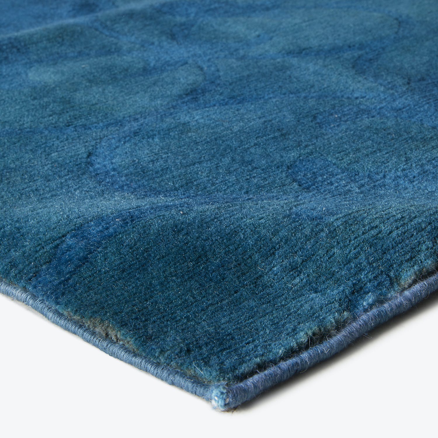 Close-up of a textured blue rug with folded hem edges.