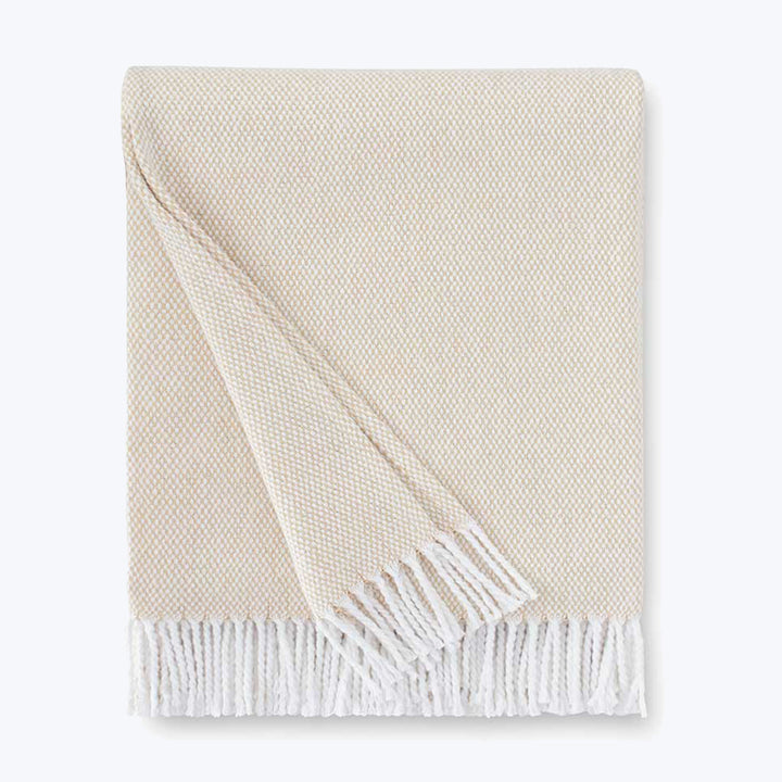 Neatly folded off-white blanket with herringbone pattern and fringe