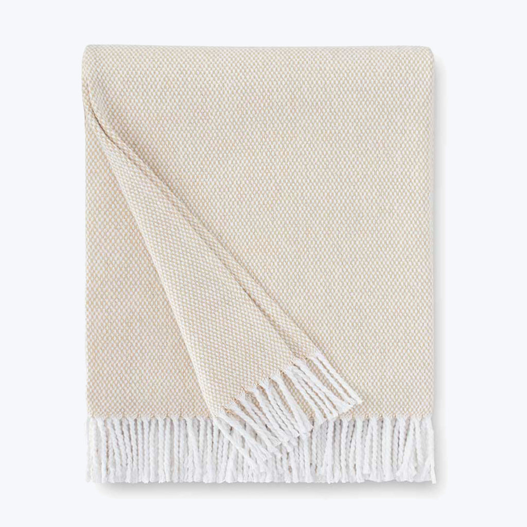 Neatly folded off-white blanket with herringbone pattern and fringe