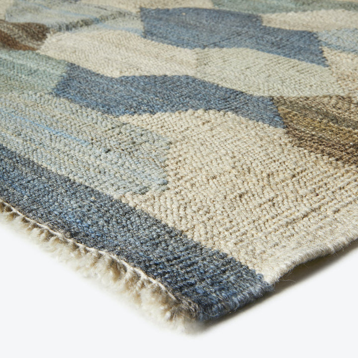 Close-up of a worn rug with a geometric blue pattern.