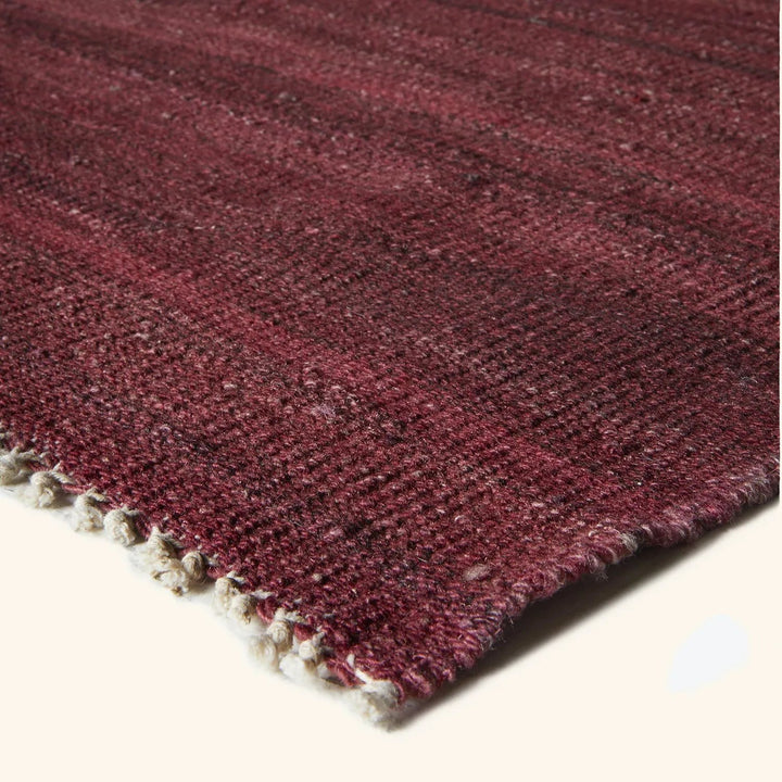 Close-up view of a hand-woven maroon rug with textured surface.
