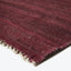 Close-up view of a hand-woven maroon rug with textured surface.