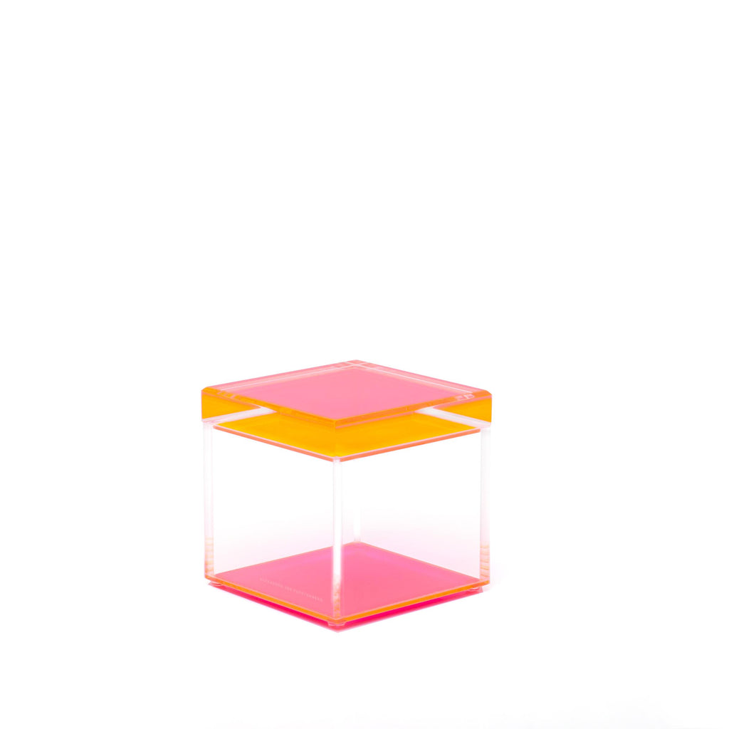 Minimalistic acrylic cube with orange and pink panels on white background.