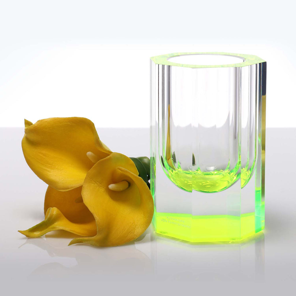 Vibrant neon glass contrasts with wilted flower on reflective surface.