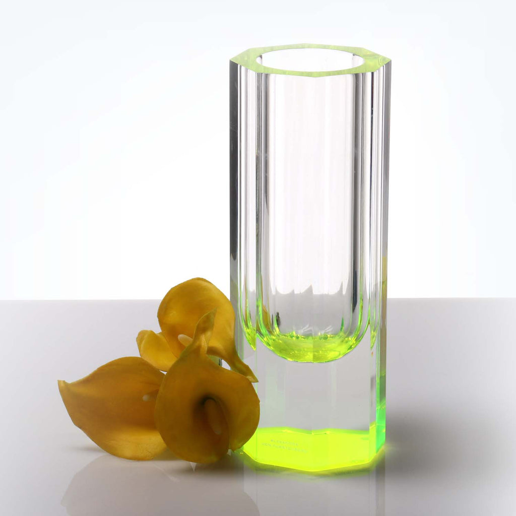 Modern green-tinted glass vase with yellow petals on white background.