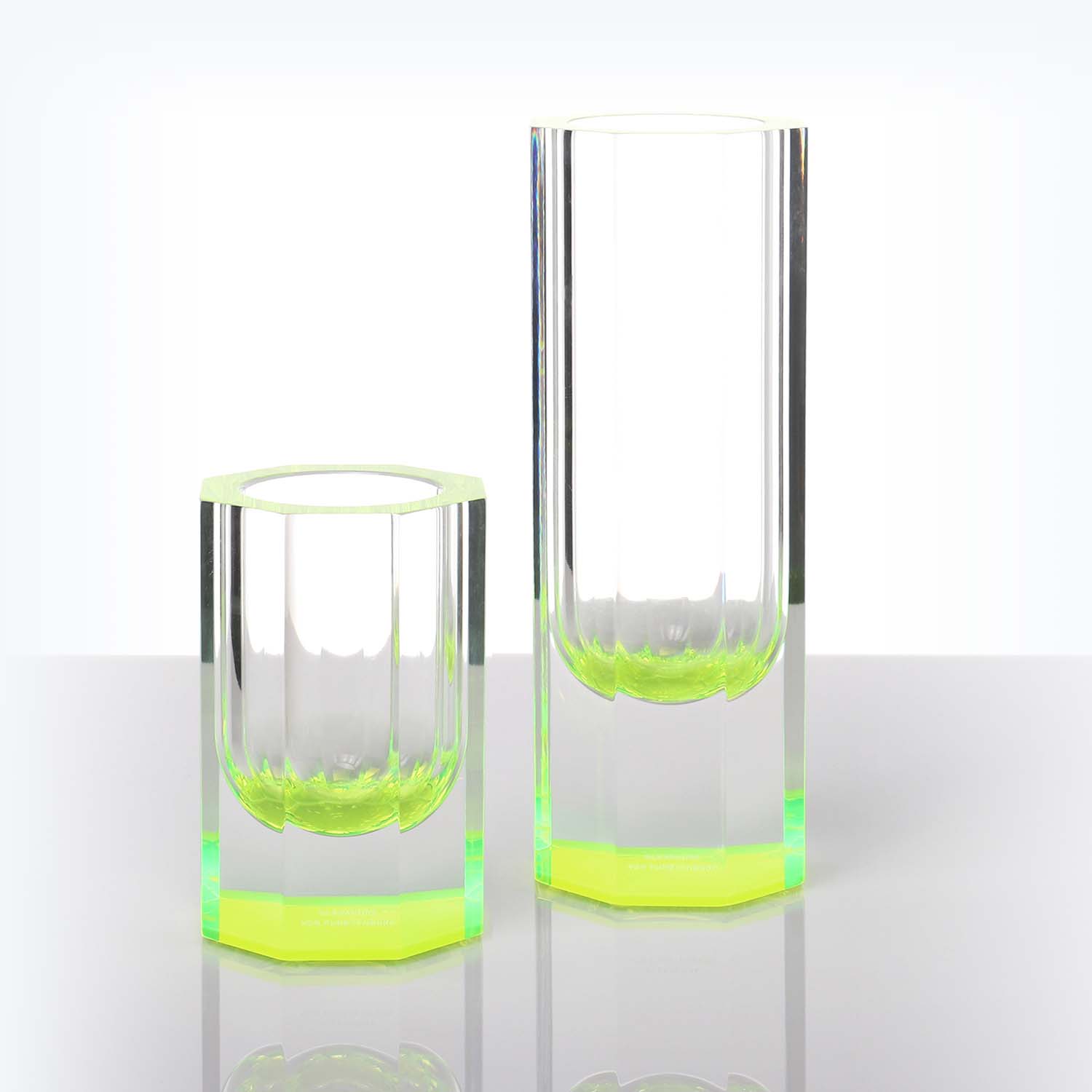 Contemporary glass tumblers with a vibrant green base on reflective surface