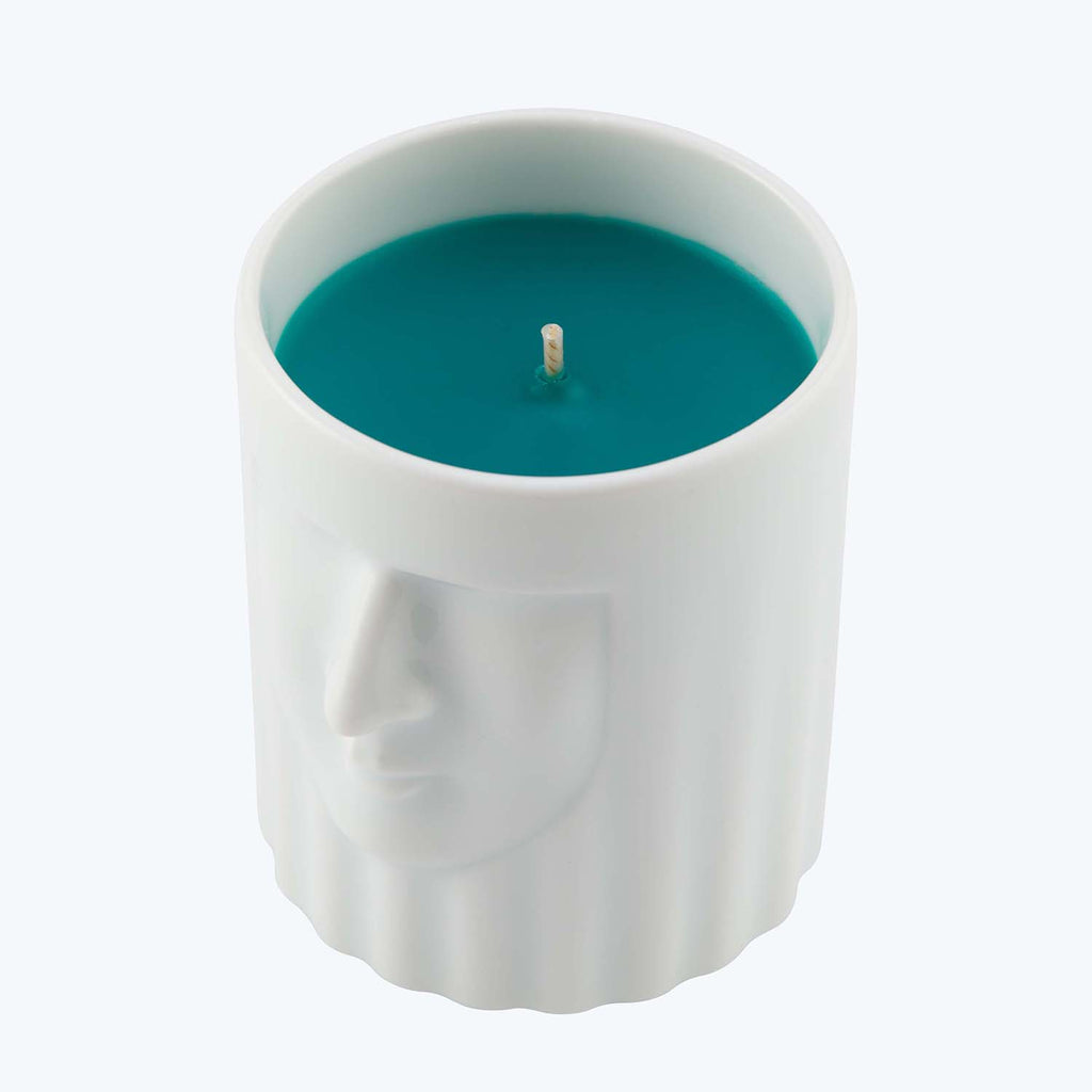 Cylindrical candle with human-like face design in vibrant teal.