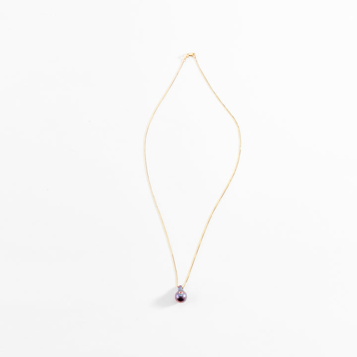 Elegant gold necklace with purple pearl pendant on white background.