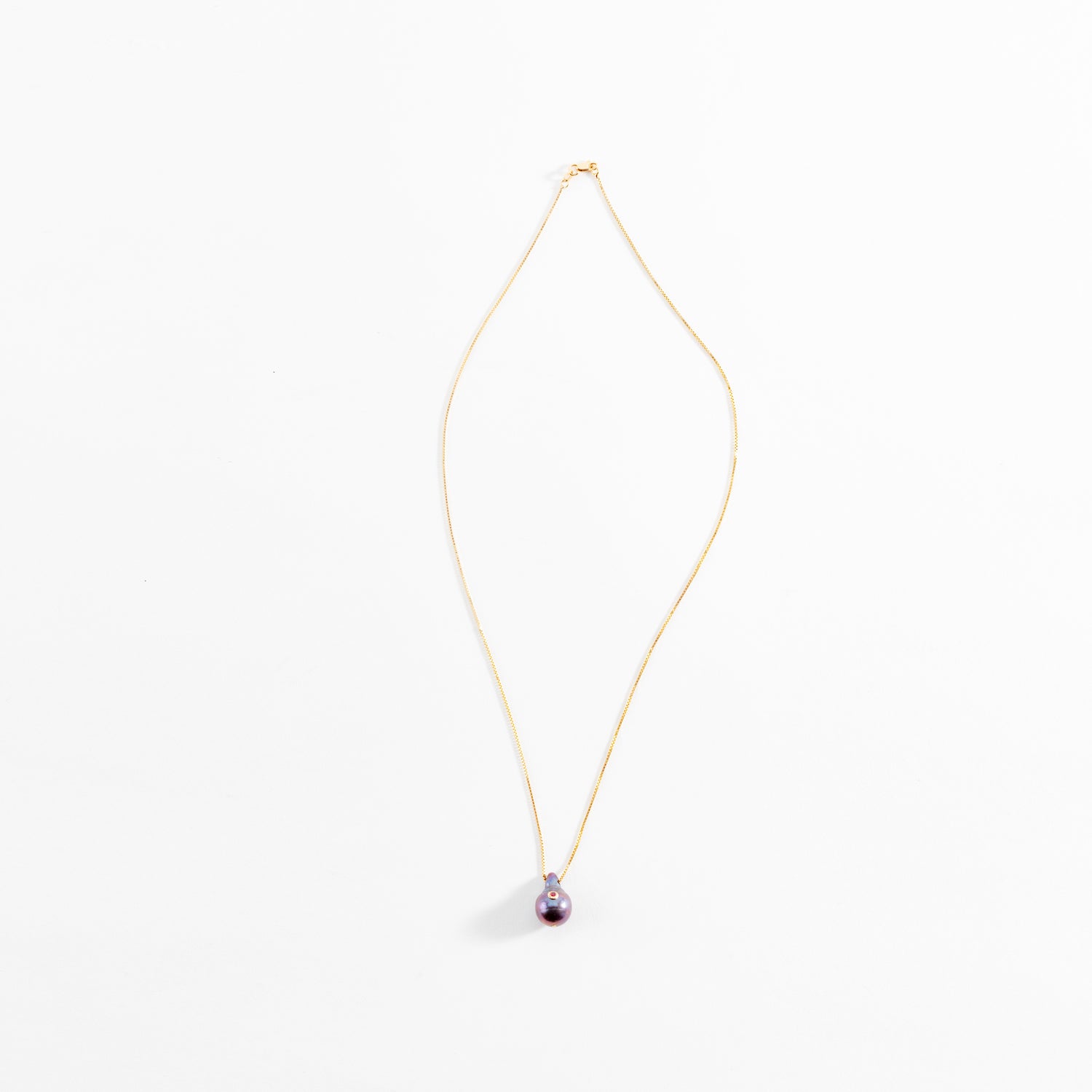 Elegant gold necklace with purple pearl pendant on white background.