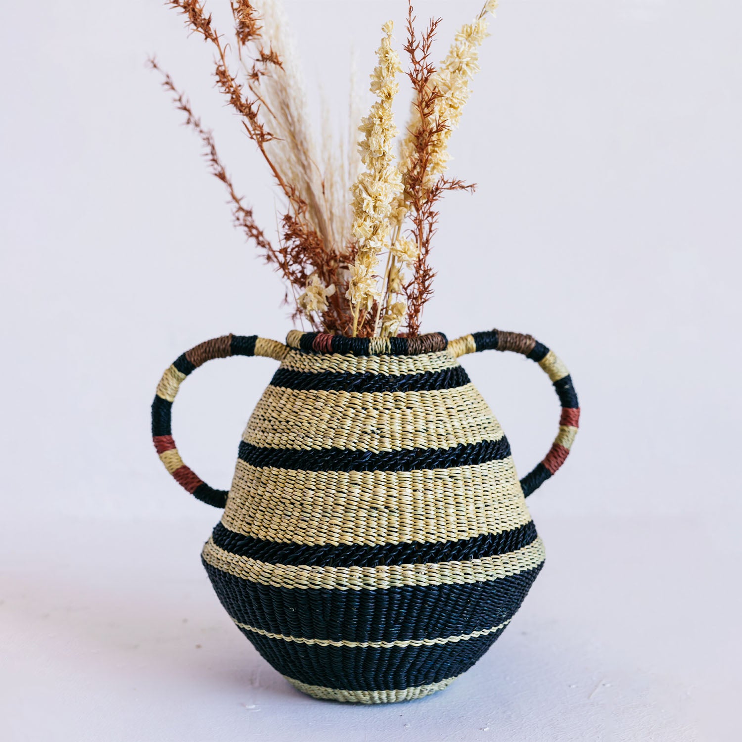 Handcrafted woven basket adorned with striped pattern holds dried flora.