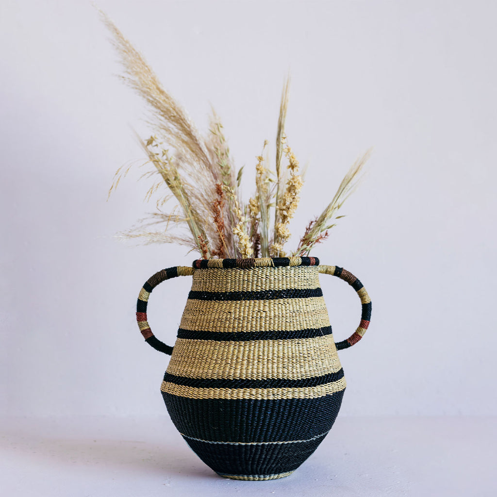 Artisanal woven vase with striped pattern and dried plant arrangement.