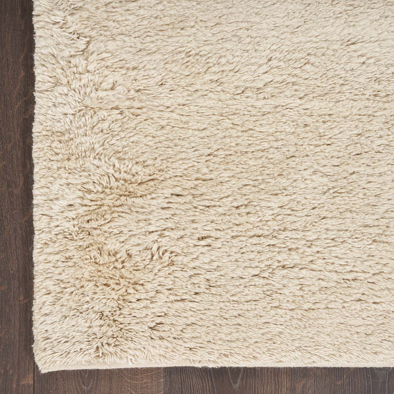 Light beige shaggy rug on dark wooden floor creates cozy ambiance.
