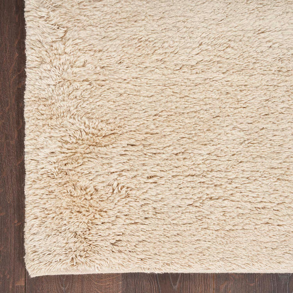 Light beige shaggy rug on dark wooden floor creates cozy ambiance.