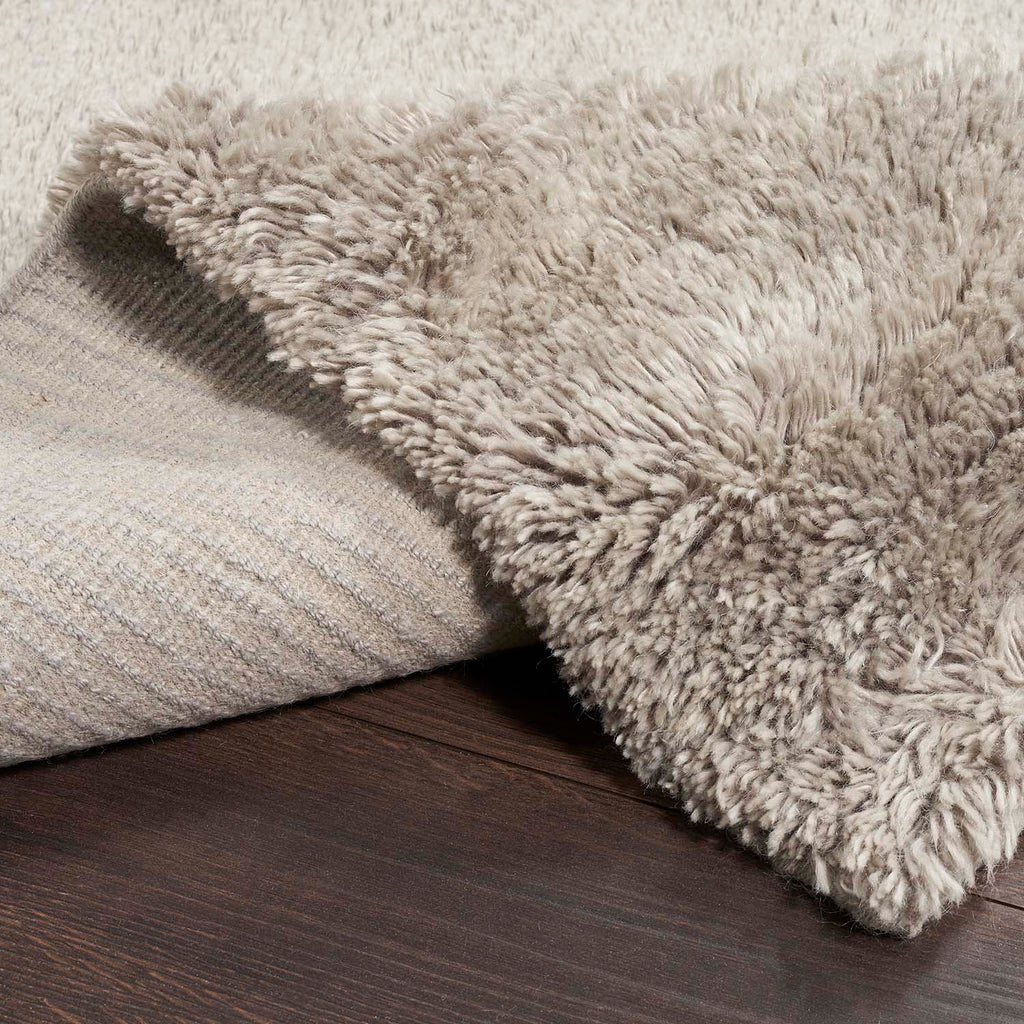 Close-up view of a shaggy rug on dark wooden floor.