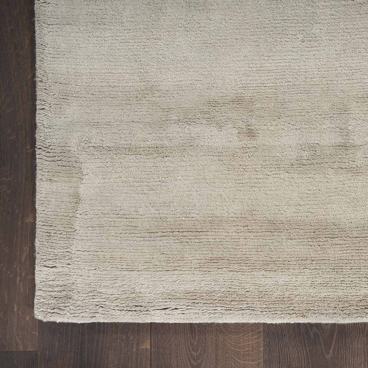 Top-down view of a plush beige area rug on dark hardwood flooring.