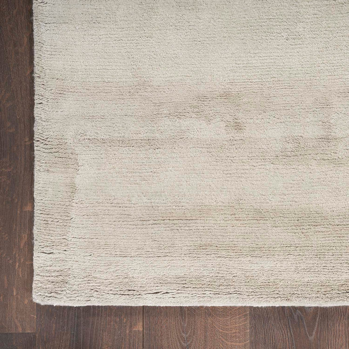 Close-up of soft, textured beige rug on dark wood floor.