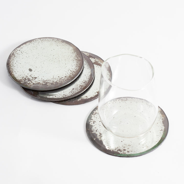 Four circular coasters with a speckled design on a white background, accompanied by an upside-down glass tumbler.