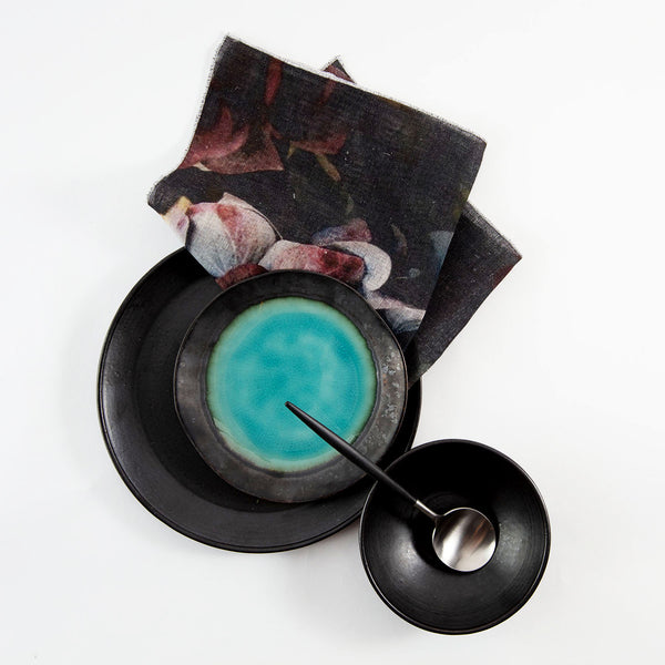 Elegant tabletop setting with dark-toned plate and vibrant turquoise circle
