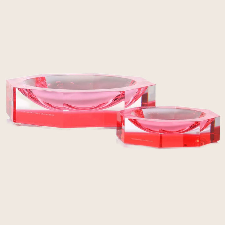 Geometric red glass bowls with glossy finish on reflective surface.