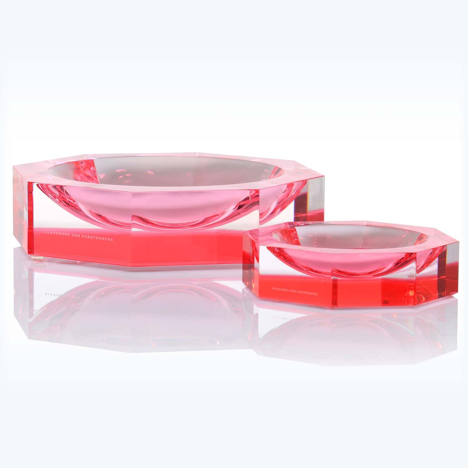 Geometric red glass bowls with glossy finish on reflective surface.