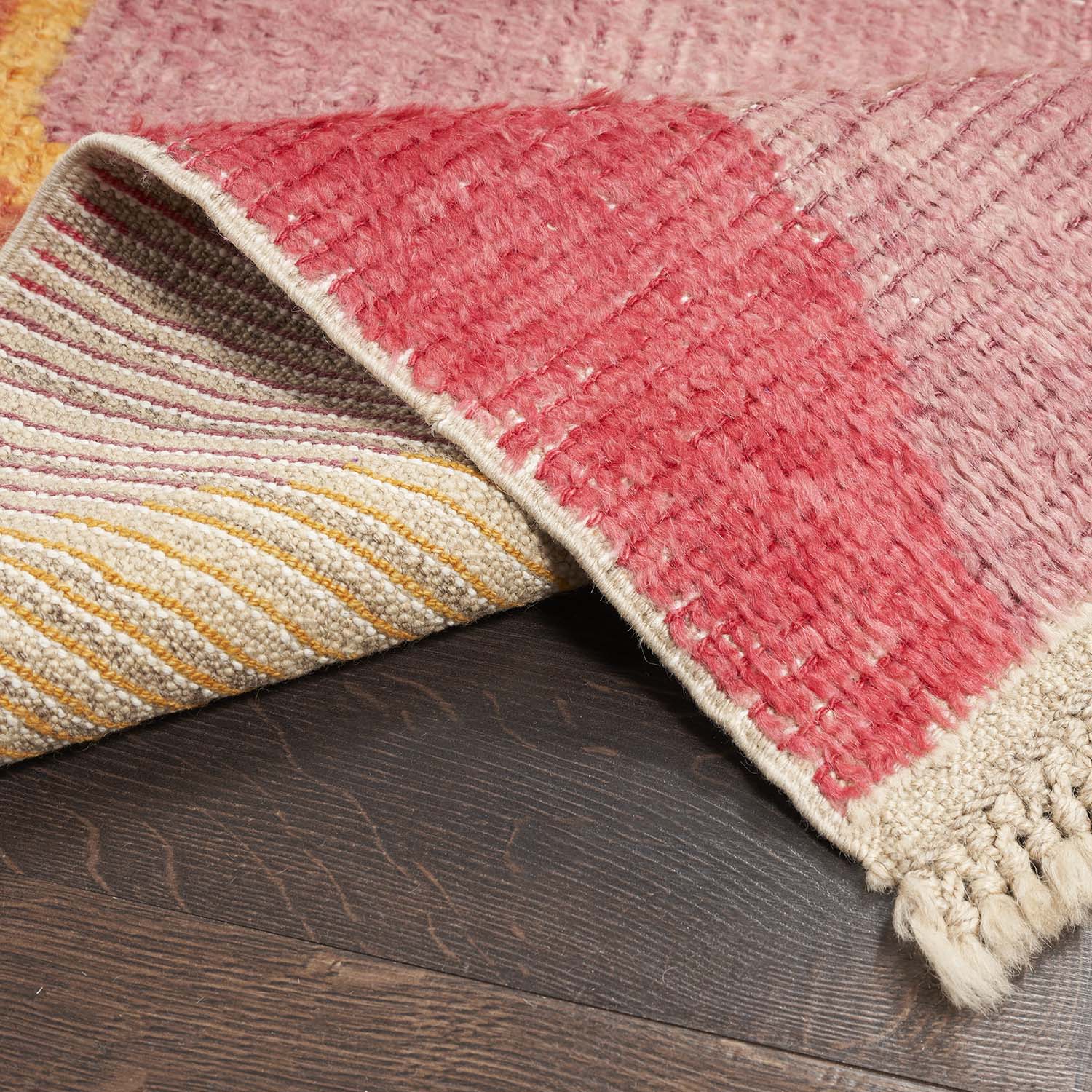 Close-up of a handwoven rug with warm-toned stripes on wood flooring