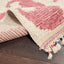 Close-up of cream and pink textured rug with tassels and vibrant thread accents