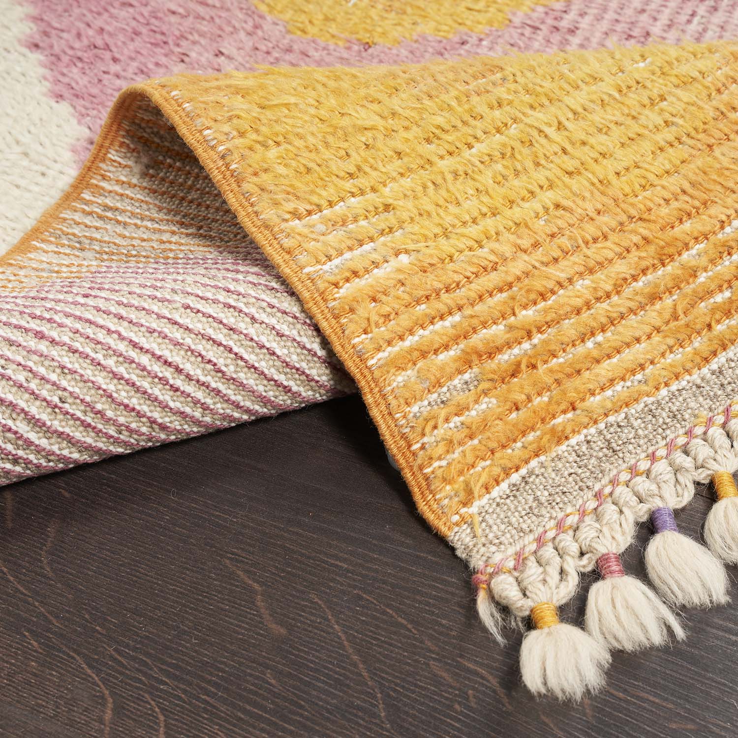 Close-up of vibrant woven rug with tassels on wooden floor.