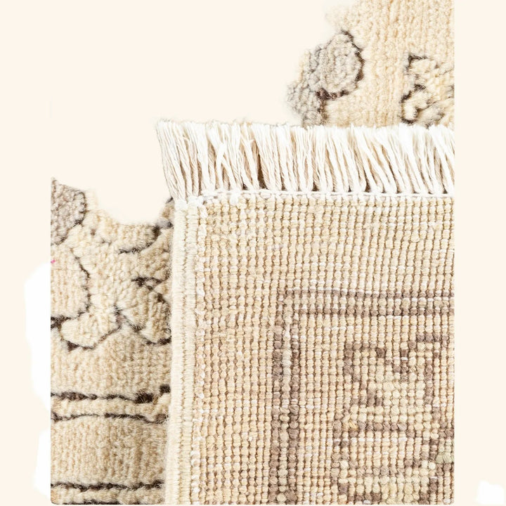 Close-up of a cream and beige woven rug with fringed border.