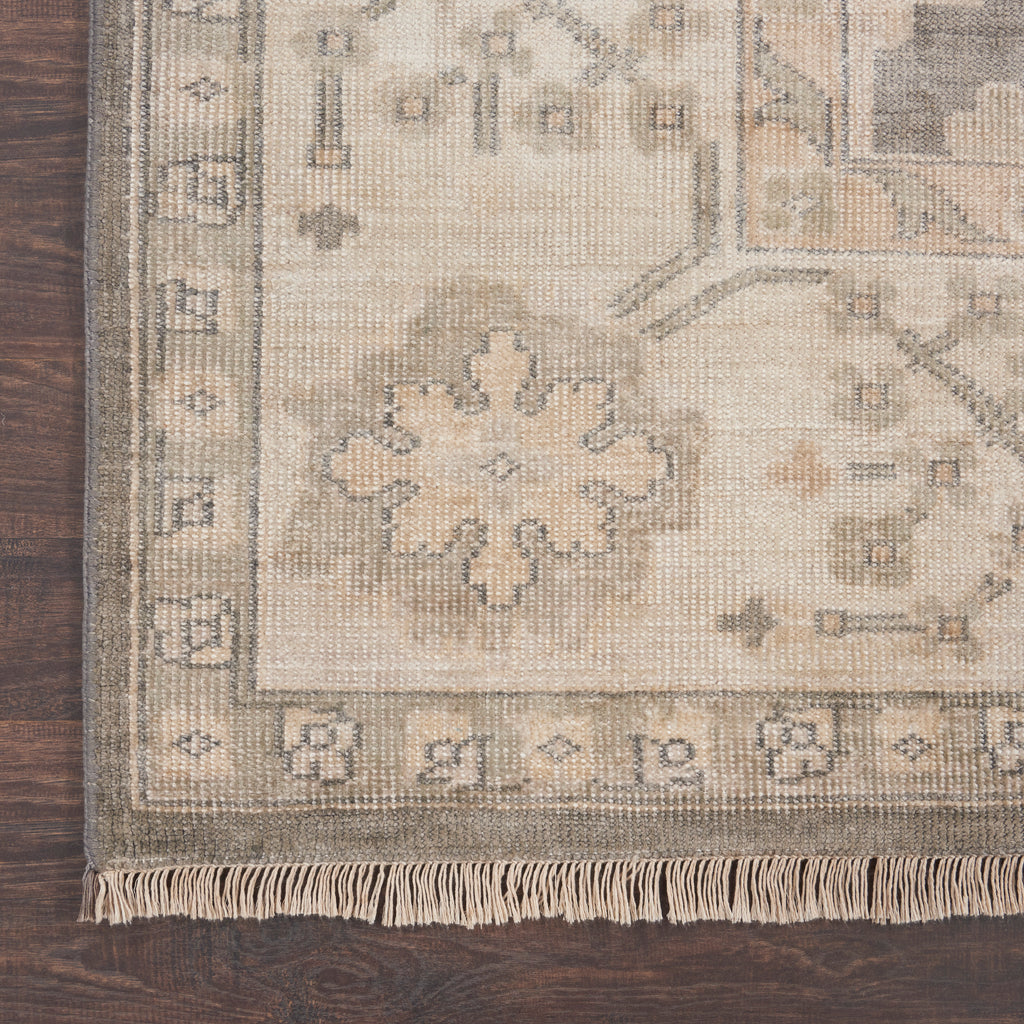 Close-up view of a neutral-tone, patterned rug on a wooden floor.