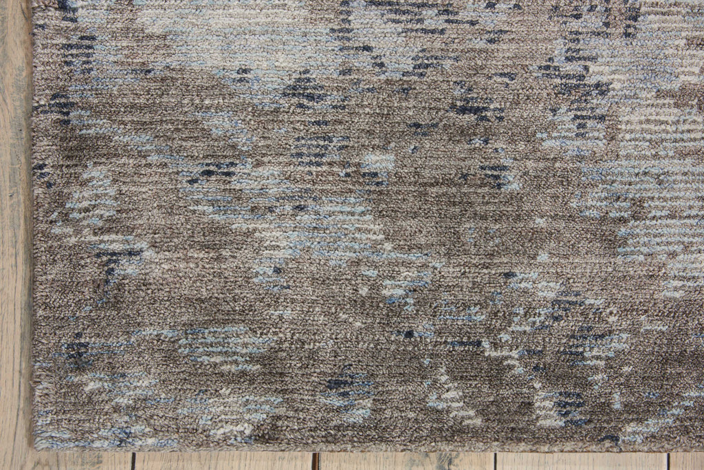 Close-up of textured area rug with brown, beige, and blue pattern on wooden floor.