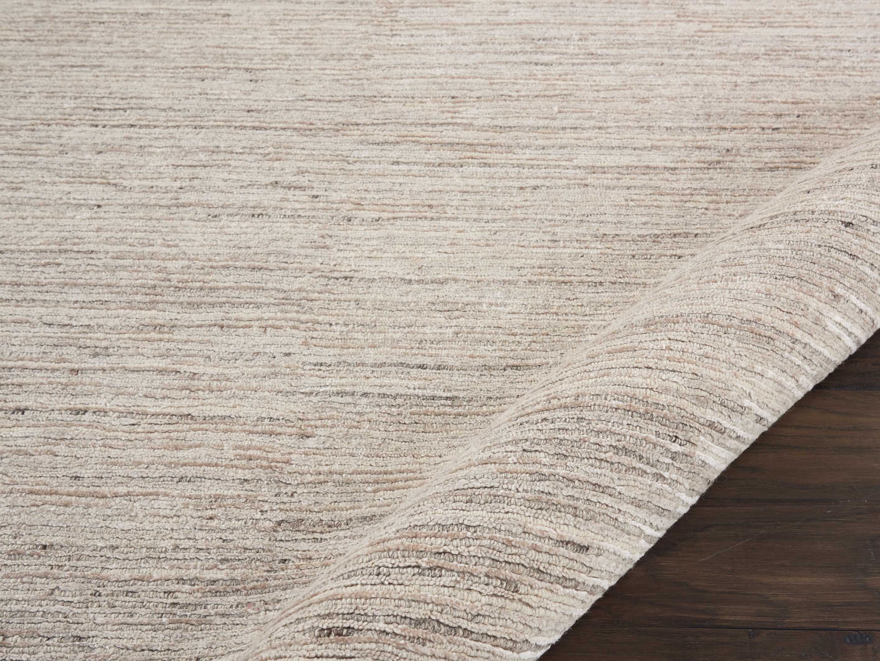 Close-up of a tightly woven beige rug on polished wood floor.