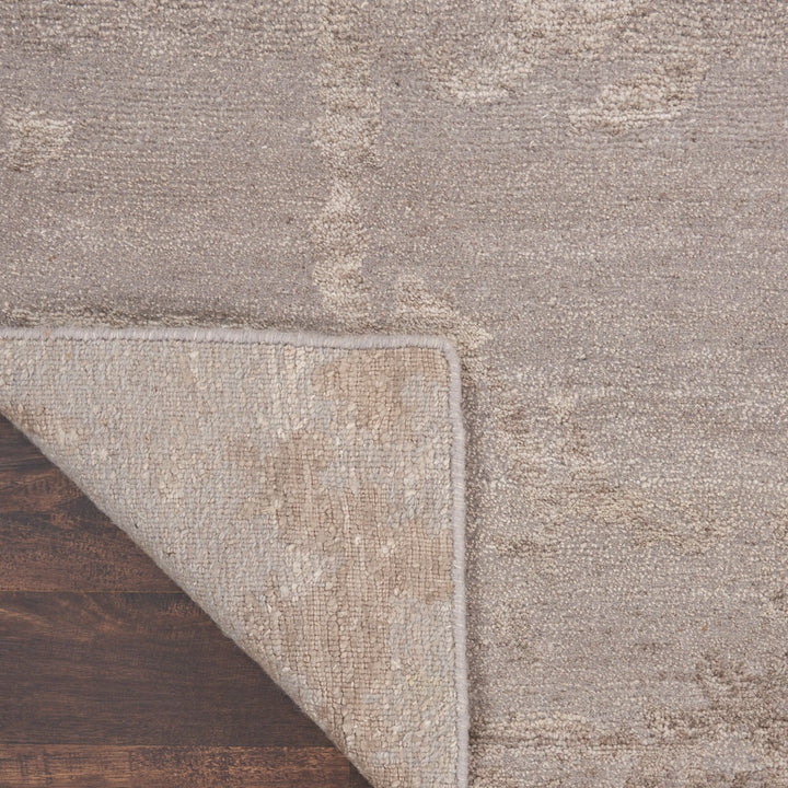 Textured area rug in light beiges and tans with speckled pattern, revealing underside on dark wood floor.