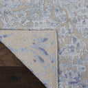 Folded corner reveals intricate blue and gray patterned rug design.