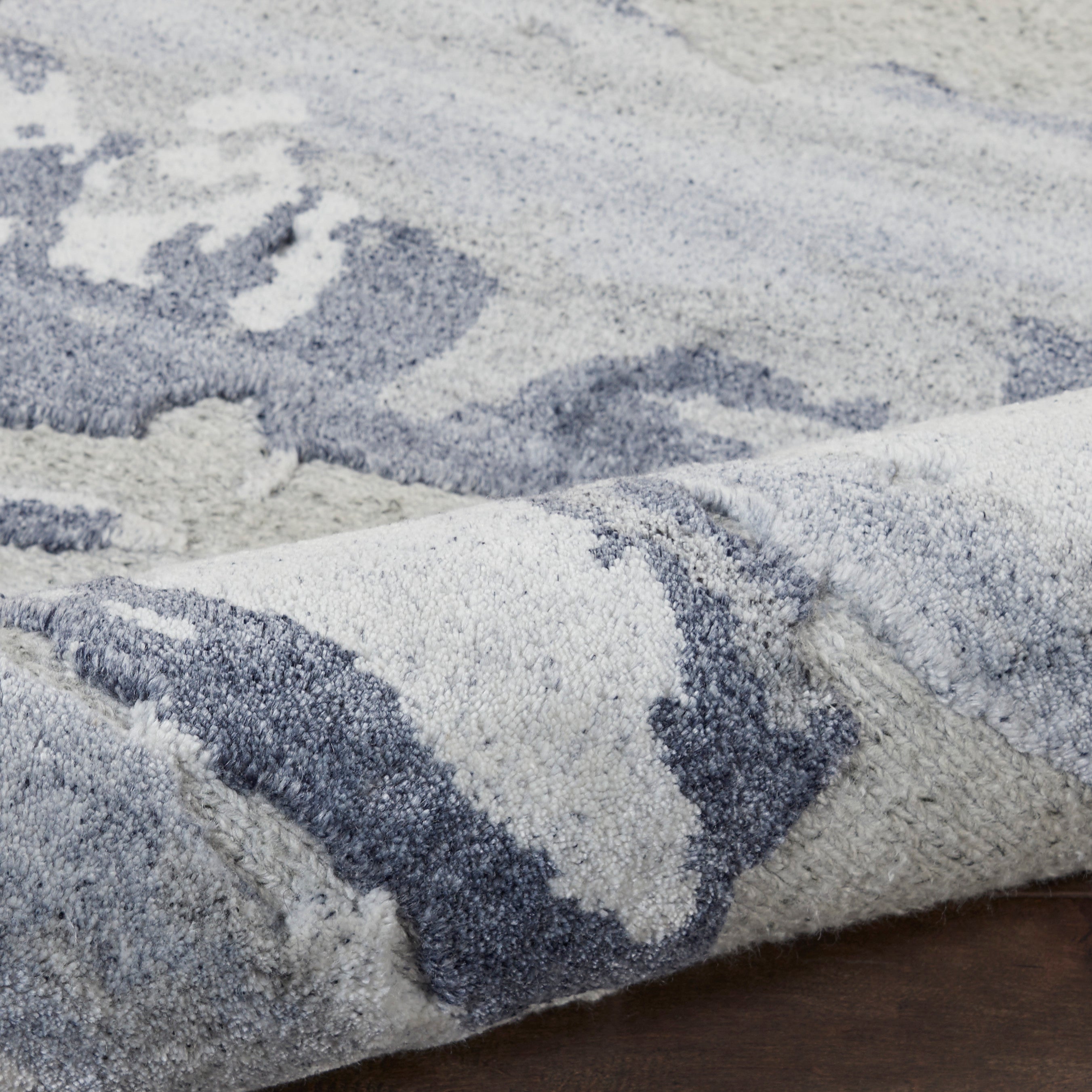 Close-up of a plush grey and blue area rug with textured patterns and soft pile, adding depth to a modern interior.