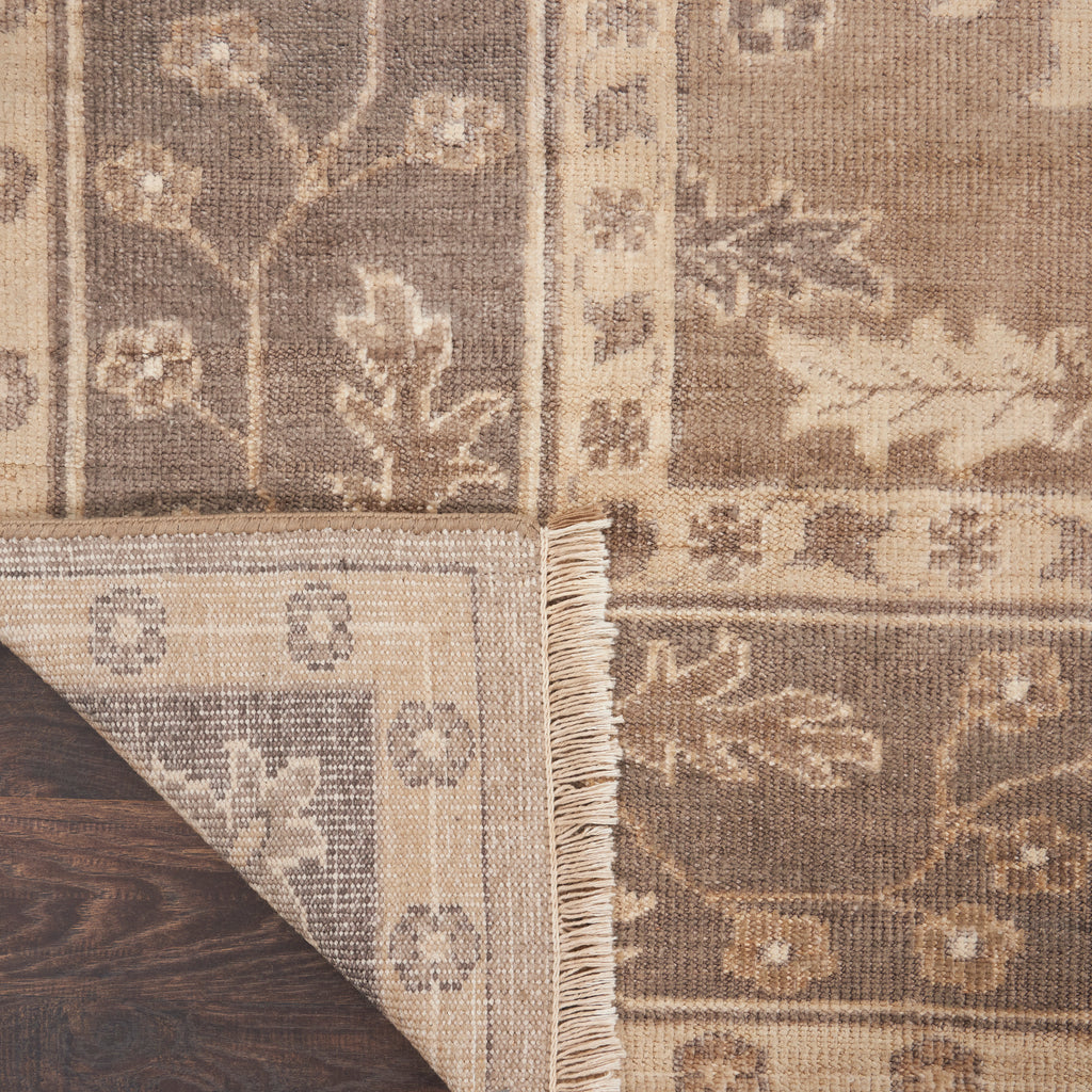 Close-up view of a patterned rug with botanical and geometric designs in beige and brown, showcasing its woven texture and fringed edges.