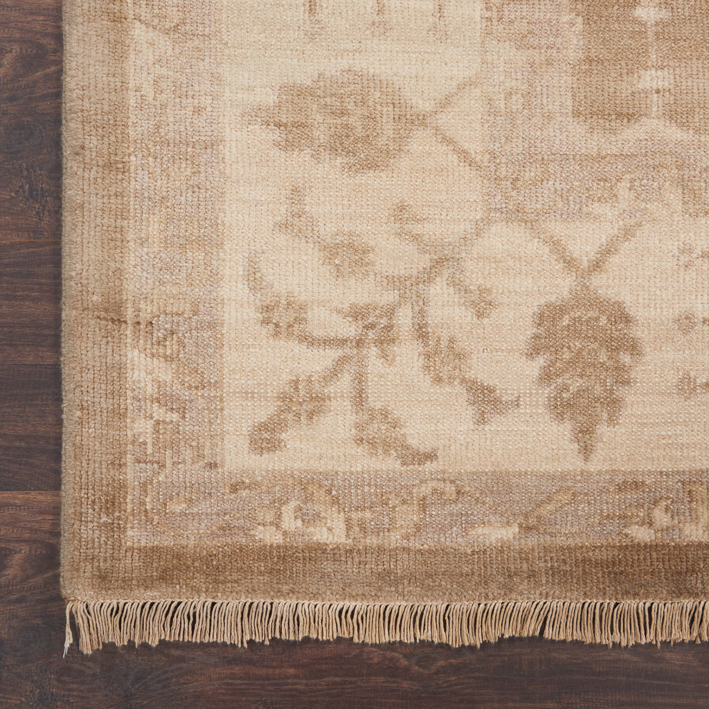 Close-up view of a floral rug with fringe on wooden floor.
