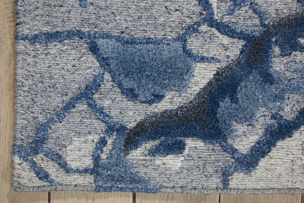 Close-up of a textured blue and grey area rug on wooden floor.