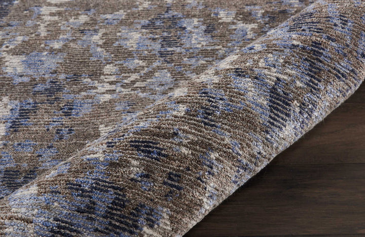 Close-up view of a textured carpet with varied brown and blue pattern on a dark wooden floor.