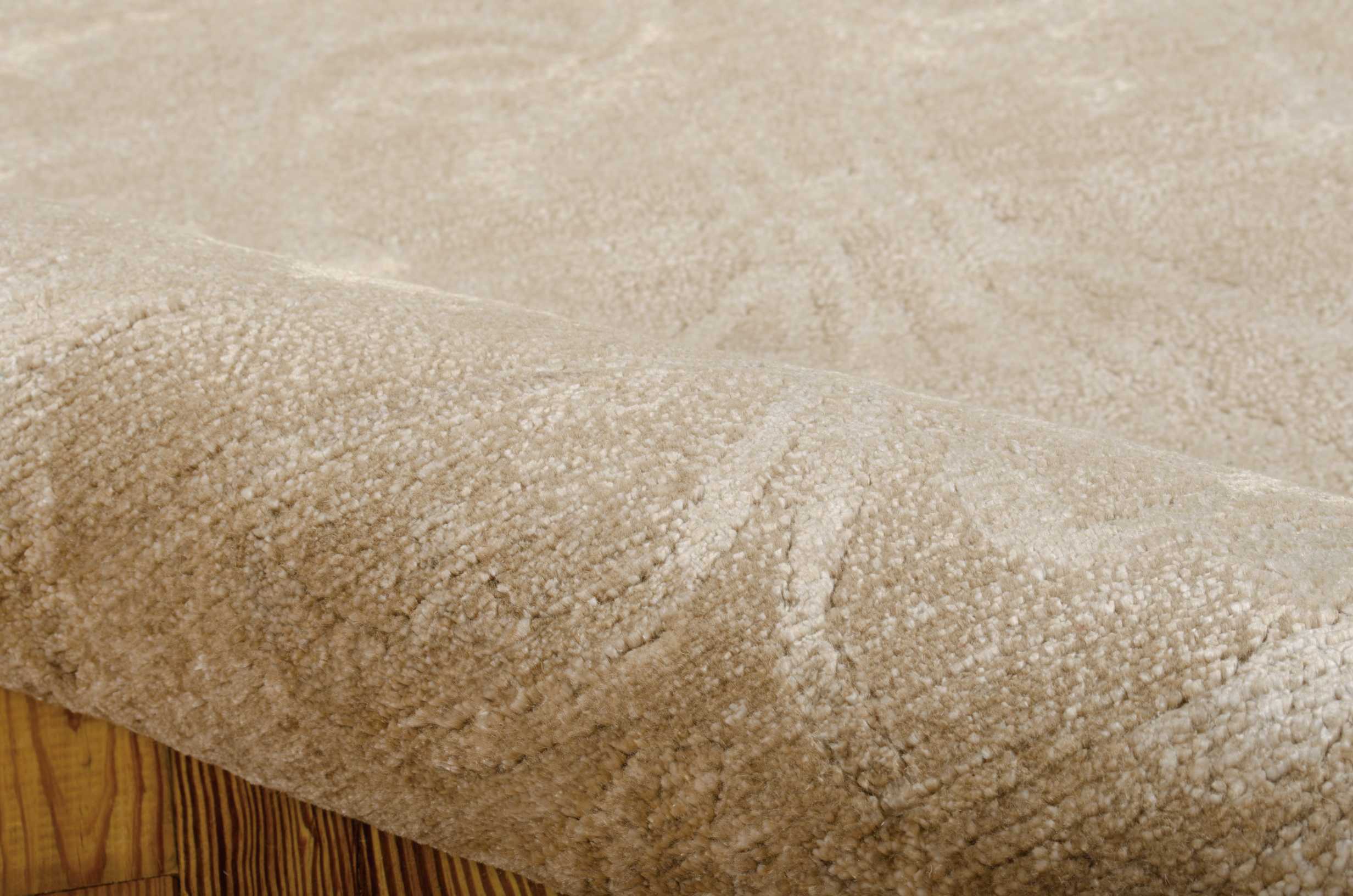Close-up view of a new, plush beige carpet over wooden floor.