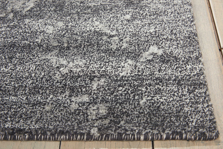 Close-up of textured area rug with grey speckled pattern on wooden floor.