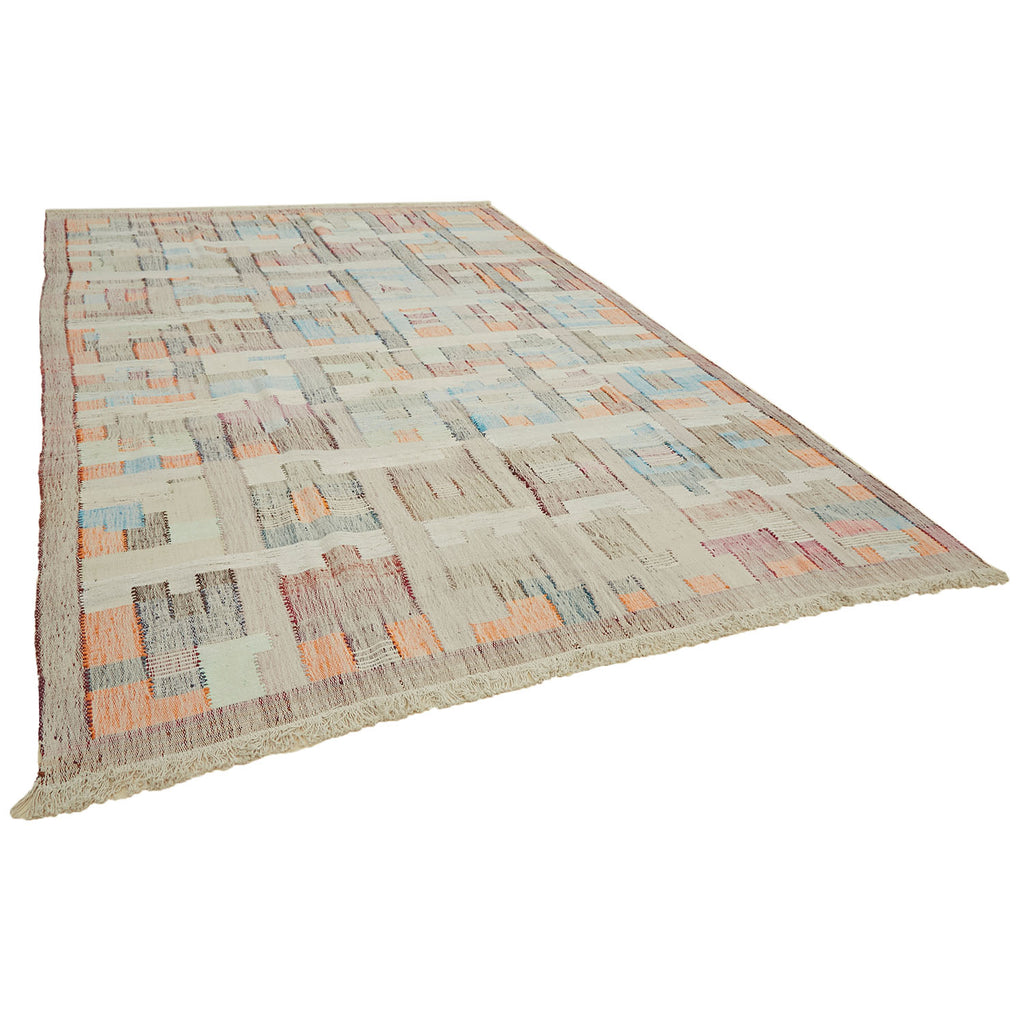 Large patchwork area rug in muted pastel tones with fringed border