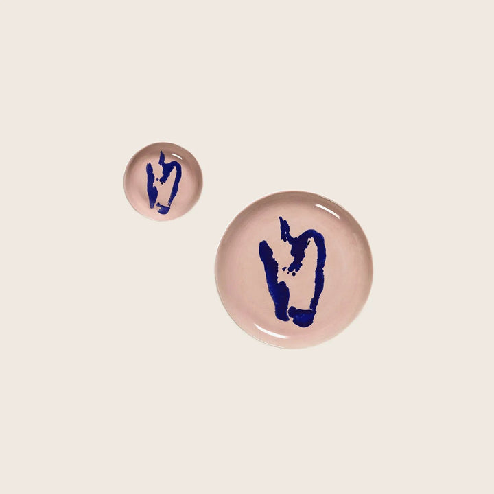 Modern ceramic plates with abstract face designs on pinkish-tan background.