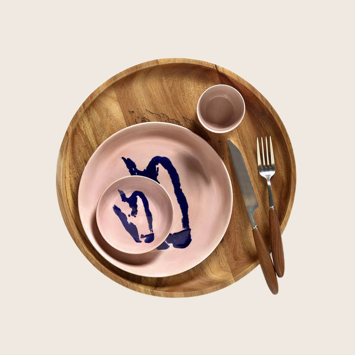 Rustic modern dinnerware setup with pink plate and wooden utensils.