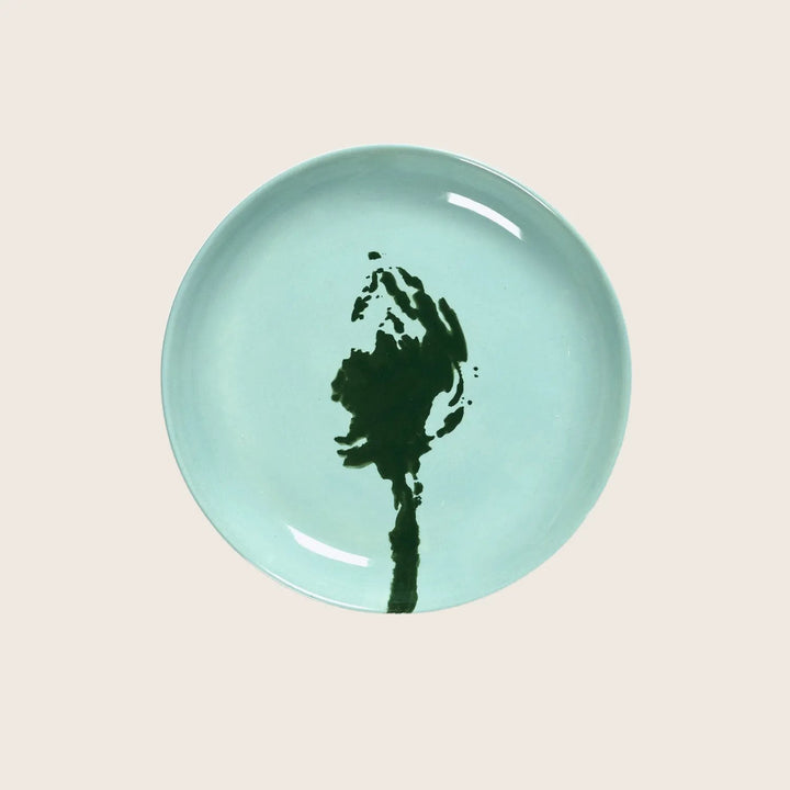 Abstract floral design on seafoam green ceramic plate, white background.