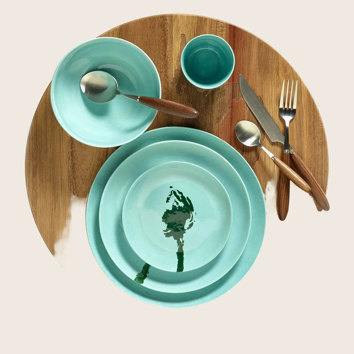 Symmetric arrangement of turquoise dinnerware on wooden placemat, minimalist setting.