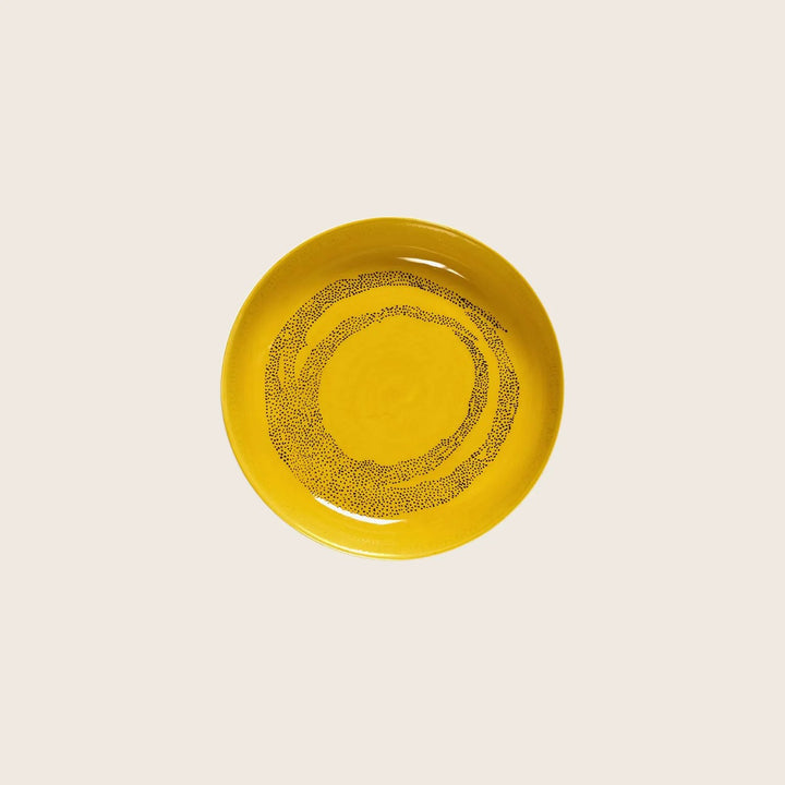 Minimalist yellow ceramic plate with black dot design, glossy finish.