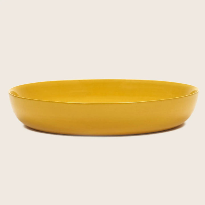 Minimalistic yellow ceramic dish with low rim on white background.