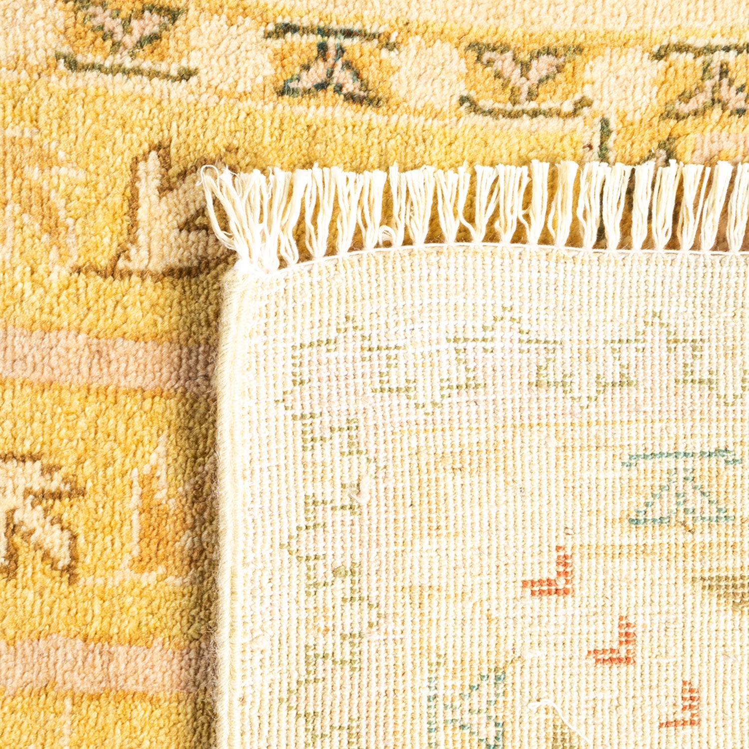 Close-up view of a woven rug with plush texture and pattern in warm yellow and green colors, transitioning to a coarser beige underside with faint traces of pattern.