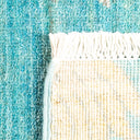 Close-up view of textile materials: dense teal carpet and loose cream fabric with fringe; contrasting textures and craftsmanship suggest handmade or unique weaving techniques.