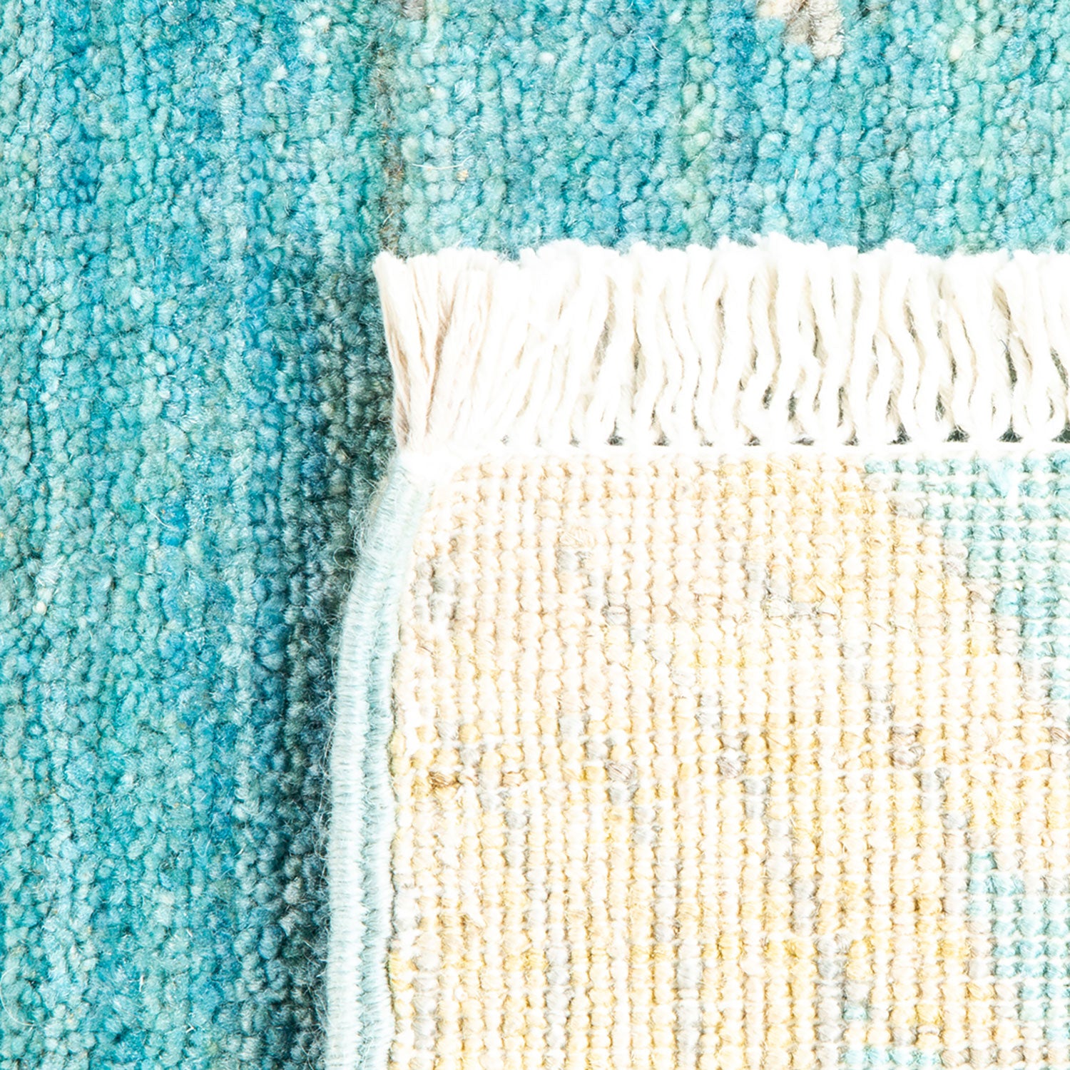 Close-up view of textile materials: dense teal carpet and loose cream fabric with fringe; contrasting textures and craftsmanship suggest handmade or unique weaving techniques.